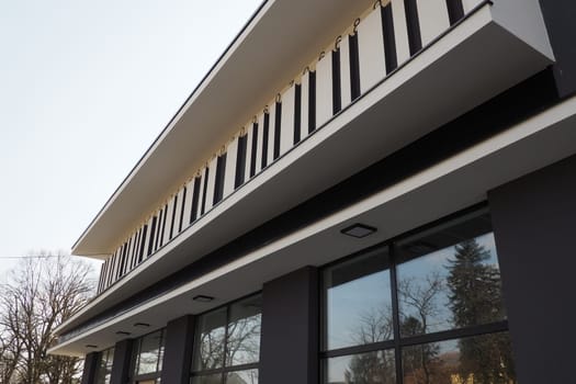 Modern building. Thuja with a shaped sheared crown. Modern landscape design. Beautiful decoration of the garden, lawn, house territory. Gray wall with striped decor, large display glass windows
