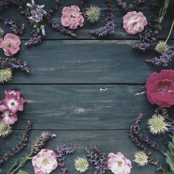 Flowers in a circle on a wooden background. Postcard for the holiday. Roses, geraniums, lavender, sage and hairy chestnuts are placed along the edges on dark boards. Background copy space, flat lay