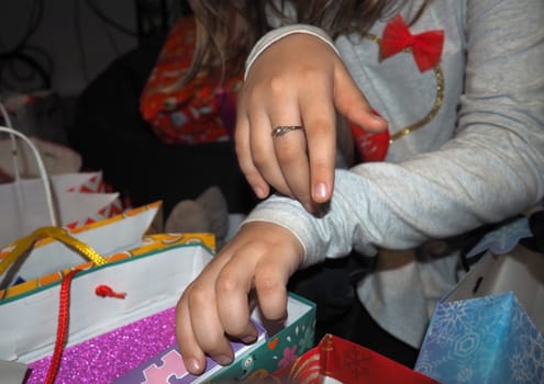 Beautiful children's hands open packages with gifts after the birthday celebration. Unpacking sale purchases or items in decorative packaging bags. Gray long sleeves