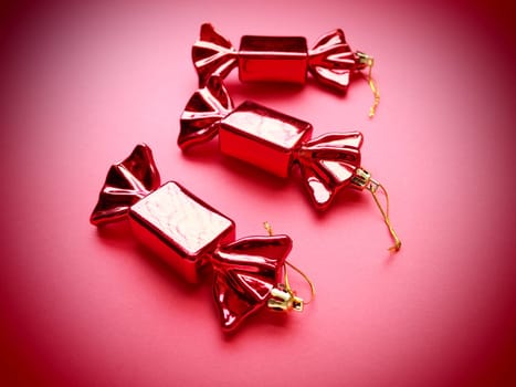 Christmas decorations in the form of sweets. Three candies in wrappers on a pink background. Beautiful decorations for New Year and Christmas. Hanging threads. Pink magenta background with vignette