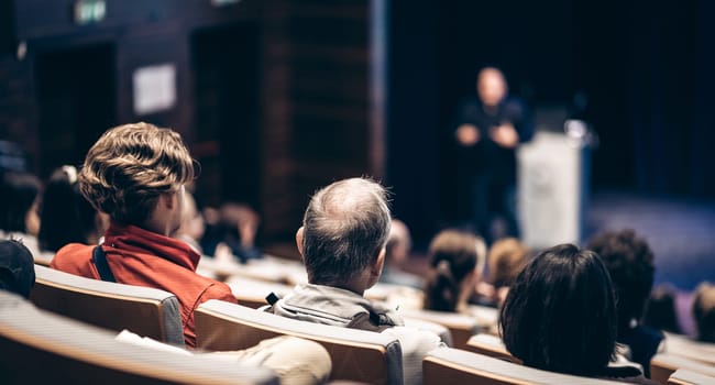 Speaker giving a talk in conference hall at business event. Rear view of unrecognizable people in audience at the conference hall. Business and entrepreneurship concept