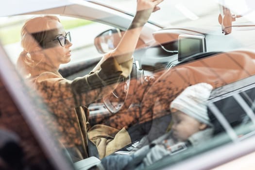 Mother concentrating on driving family car running errands while her baby sleeps in infant car seat by her site