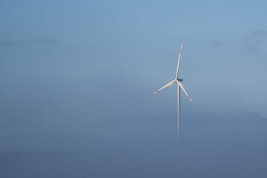 Windmill in foggy landscape. Renewable energy for environmentally conscious future. Power generation that is important for climate change.