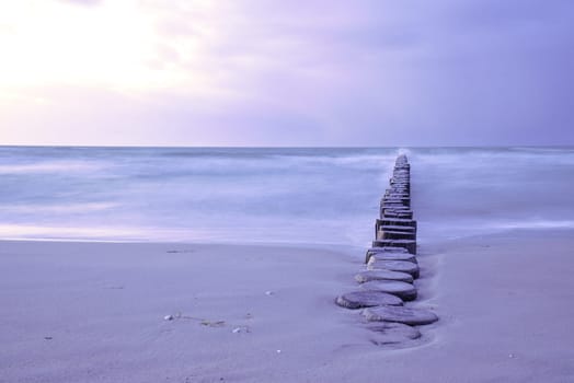 Groynes protruding into the horizon in the Baltic Sea. Long exposure with muted colors. Landscape shot by the sea