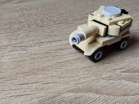 Toy tank on a wooden table. Plastic toy. Craft from a childrens designer. The beige color of the tank, a defocused image around the edges. Lesson that develops the fine motor skills of the childs hands and fingers