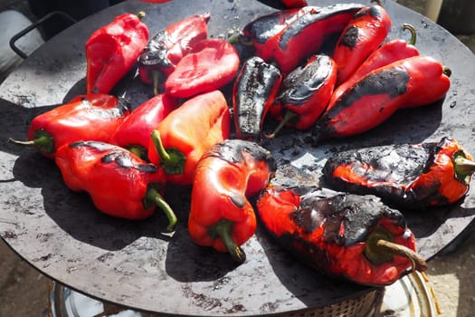 Roasting red peppers for a smoky flavor and quick peeling. Thermal processing of the pepper crop on metal circle. Brazier container used to burn charcoal fuel for cooking, heating or cultural rituals