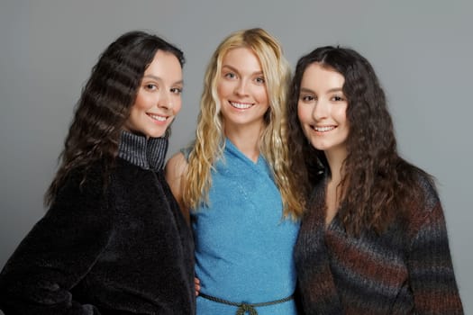 Three attractive girls in woolen coats posing in studio. Happy smiling friends. Natural makeup.