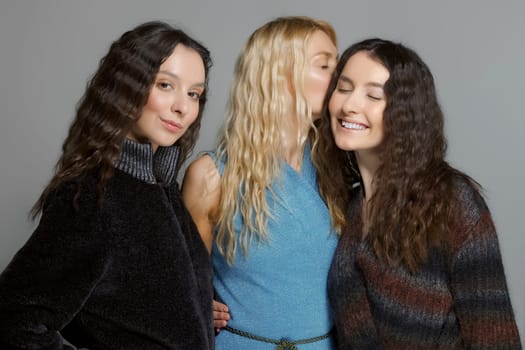 Three attractive girls in woolen coats posing in studio. Gossip girls.