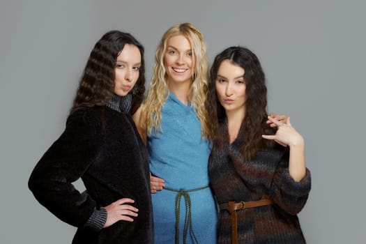 Three attractive girls in woolen coats posing in studio. Happy smiling friends. Natural makeup.