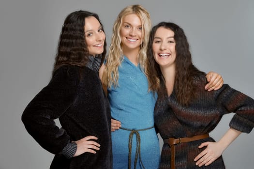 Three attractive girls in woolen coats posing in studio. Happy smiling friends. Natural makeup.