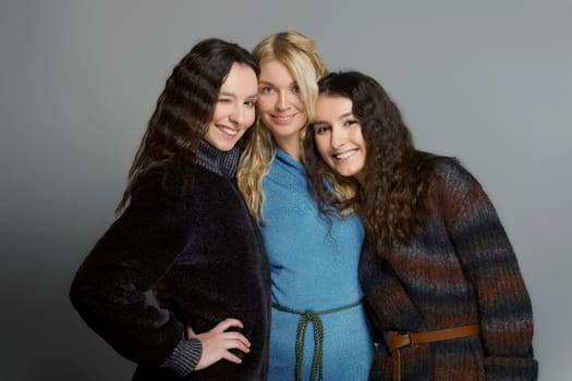 Three attractive girls in woolen coats posing in studio. Happy smiling friends. Natural makeup.