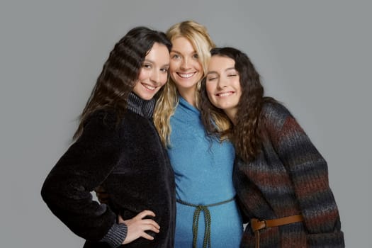 Three attractive girls in woolen coats posing in studio. Happy smiling friends. Natural makeup.
