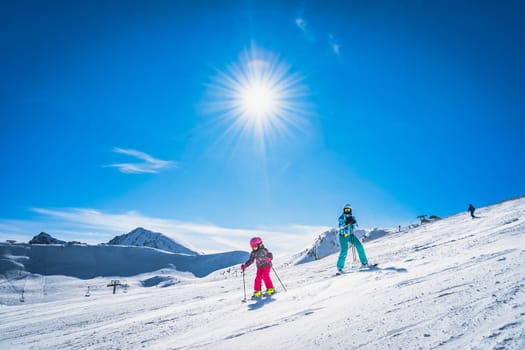 Mother teaching daughter how to ski, skiing down on a ski slope. Sunny day on ski winter holidays in Andorra, El Tarter, Pyrenees Mountains