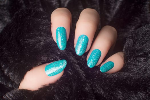 Female hand with glittered white blue nails is holding black fur, manicure and nail care concept.