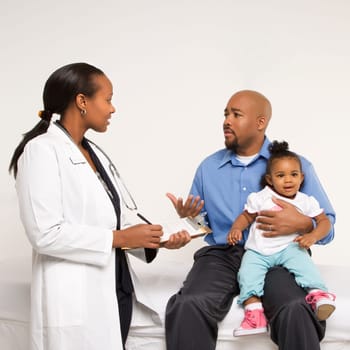 African-American father holding baby girl talking to female pediatrician.