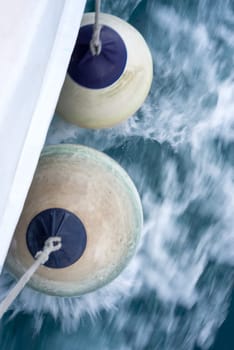 Two white fenders suspended between a boat and dockside for protection. Maritime fenders