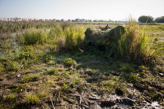 wildlife photographer hiding in a hide from camouflage netting in summer nature. Green tent for taking picture of wild animals in water environments.