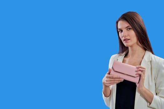 A beautiful young woman is holding a pink purse on a blue background, copy space. High quality photo