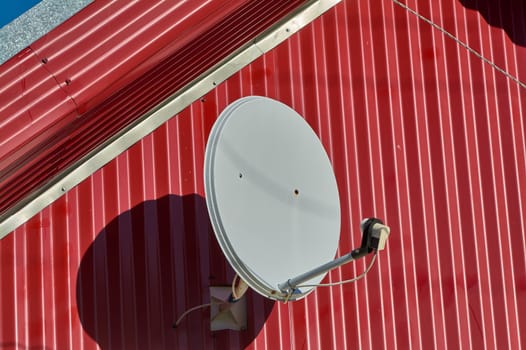 A satellite dish is hanging on the wall of the house. High quality photo