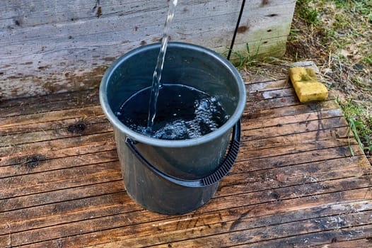 a black plastic bucket is filled with water from the pump. High quality photo