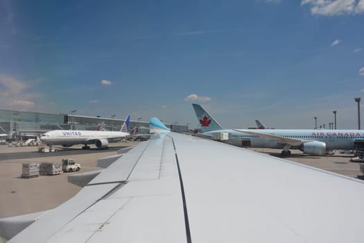 Frankfurt Airport Germany August 02, 2022 - View from the aircraft window onto a wing and a view of the terminal, a United machine being towed to the runway and an Air Canada machine being loaded