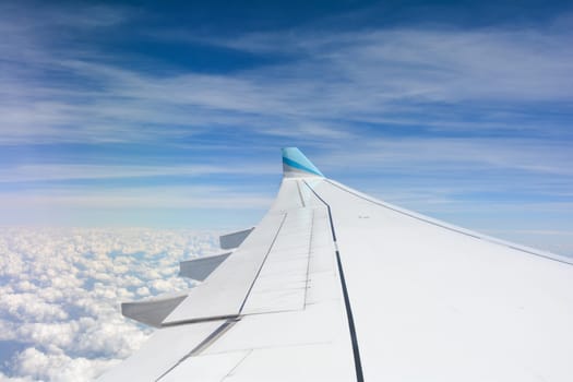 Looking out of an airplane window showing a plane wing with blue sky and white clouds