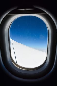 Window of an airplane showing the wing and the blue sky