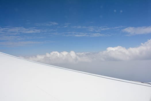 Looking out of an airplane window showing a plane wing with blue sky and white clouds
