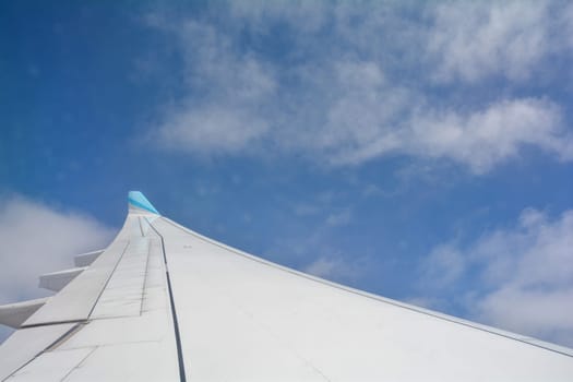 Looking out of an airplane window showing a plane wing with blue sky and white clouds
