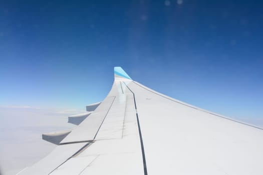 Looking out of an airplane window showing a plane wing with blue sky and white clouds
