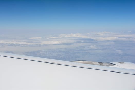 Looking out of an airplane window showing a plane wing with blue sky and white clouds