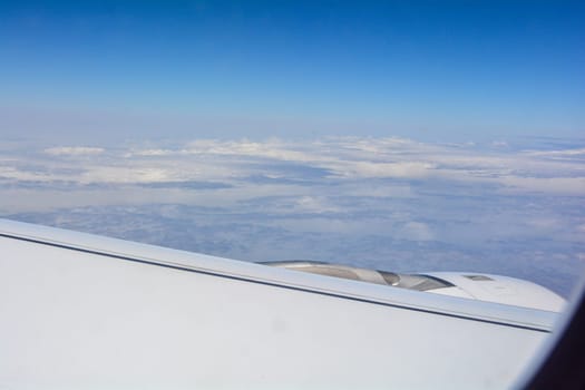 Looking out of an airplane window showing a plane wing with blue sky and white clouds
