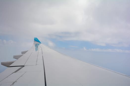 Looking out of an airplane window showing a plane wing with blue sky and white clouds