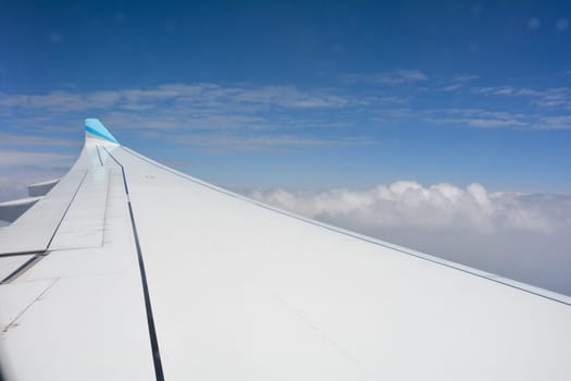 Looking out of an airplane window showing a plane wing with blue sky and white clouds
