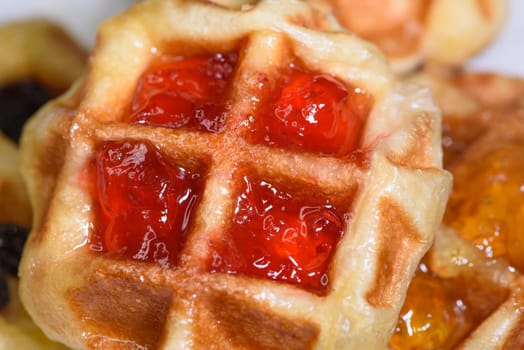 Close up of fresh waffles topped with delicious sweet strawberry jam and pineapple jam on top. Make homemade food or snacks at home