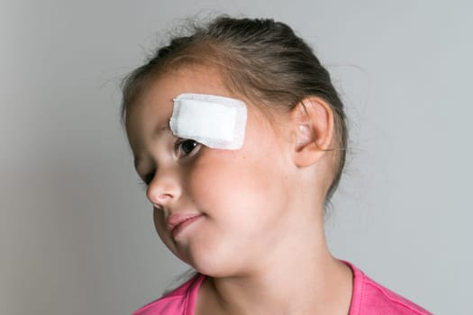 Close up brave, nice, lovely, adorable dark haired little child, girl with patch bandage on face, showing to camera. Kid protection and safety, healthcare and medicine. Child abuse and physical wounds