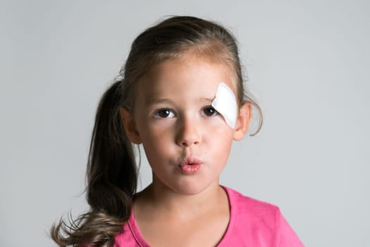 Close up cute, sad, disappointed dark haired little kid, girl with injury, scratch and patch plaster on face, making lips into tube and looking at camera. Active dangerous game and play. Children care
