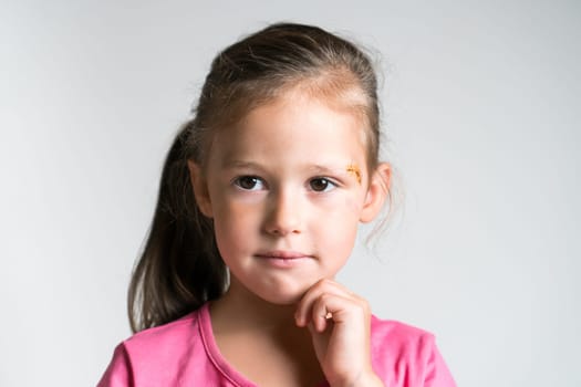 Close up pensive, lovely blond little child, girl with injury, scratch with iodine on face on white background. Child abuse, physical wounds. Social issue, family relationship difficulties. Copy space