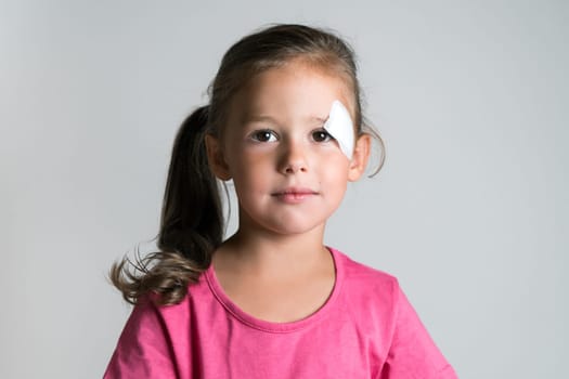 Close up nice, cute, lovely, adorable dark haired little child, girl with bandage covering injury, scratch on face. Child abuse and physical wounds. Poor children and family problems, social issues