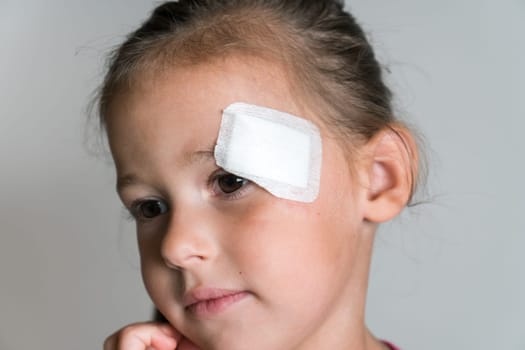 Close up brave, nice, lovely, adorable dark haired little child, girl with patch bandage on face, showing to camera. Kid protection and safety, healthcare and medicine. Child abuse and physical wounds