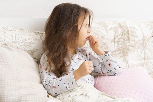 Poor, unfortunate little brunette preschooler child, girl in pajamas coughing, lying in soft bed. Sore throat, angina, tonsillitis. Recovering, health care, home treatment and bed rest. Copy space