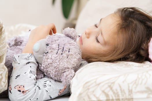 Nice little dark haired girl sleep, stroking and embracing the best furry friend, teddy bear toy in bed. Calm and deep sleep at home. Cozy comfortable atmosphere at home, napping and relaxing