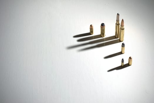 Bullets of different calibers standing on a white surface with dark, dramatic shadows.