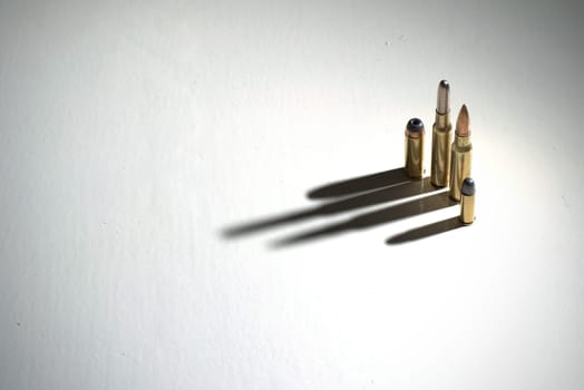 Bullets of different calibers standing on a white surface with dark, dramatic shadows.