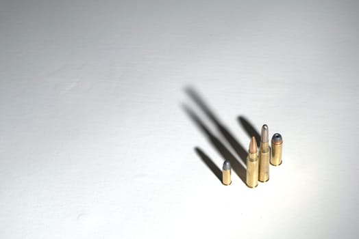 Bullets of different calibers standing on a white surface with dark, dramatic shadows.
