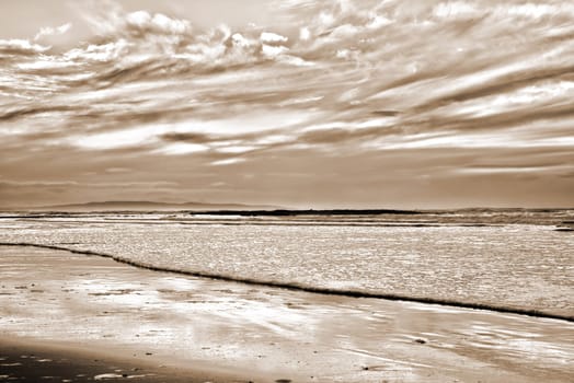 reflections and calm waves crashing onto the beach at ballybunion in ireland in sepia