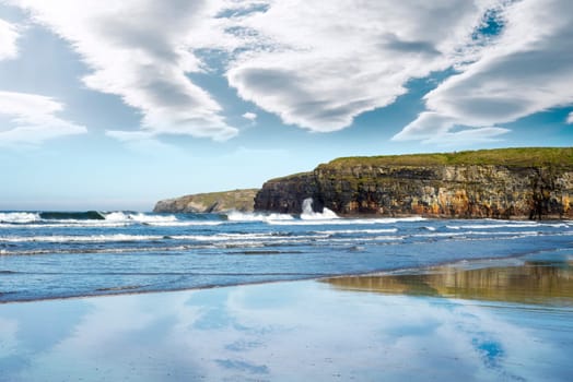 reflection of cliffs and clouds on a wet sandy ballybunion beach in ireland