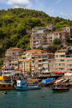 View from the sea of the green mountains of the Europian side of Bosphorus strait, with docked boats, traditional houses and dense trees in a summer day, Istanbul, Turkey