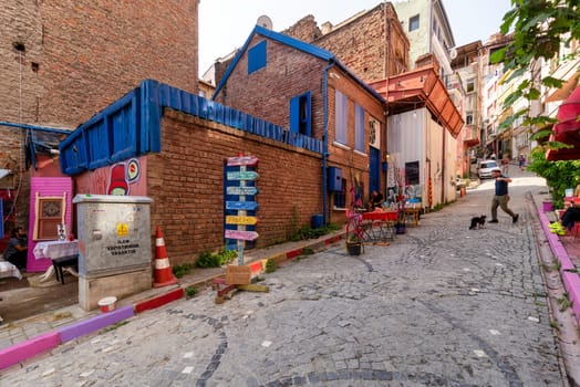 Istanbul, Turkey - August 28, 2022: Alley with cobblestone floor, and red stone bricks old buildings in old Balat district, with local pedestrians in a summer day
