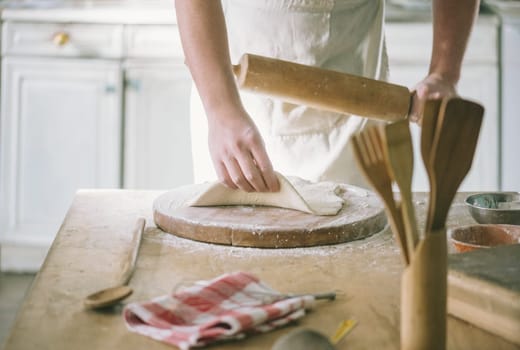 Man rolling and baking homemade dough in the kitchen. Closeup on baker's hands preparing loaf of bread. Cooking and food preparation at home.